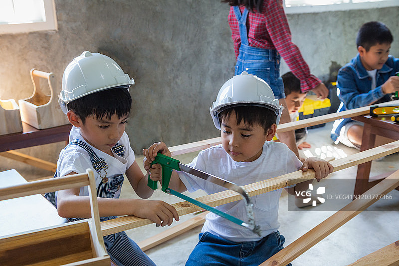 一群亚洲的木匠孩子，戴着安全帽在木工或车间里锯木板图片素材