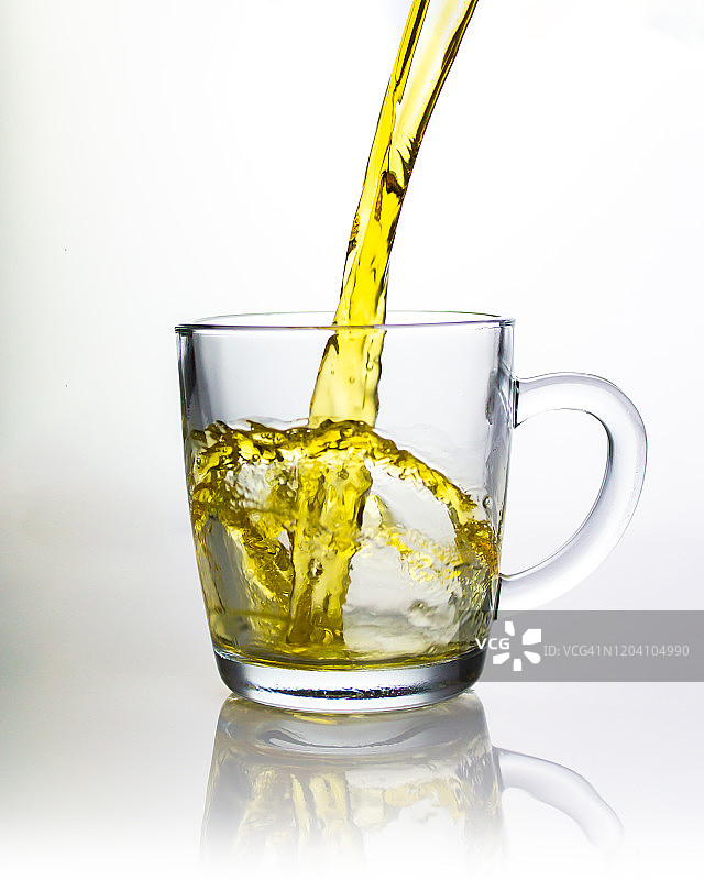 一抹绿茶洒在透明的玻璃杯里，美丽的浪花飞溅成一个弧形，倒出茶液饮料。图片素材