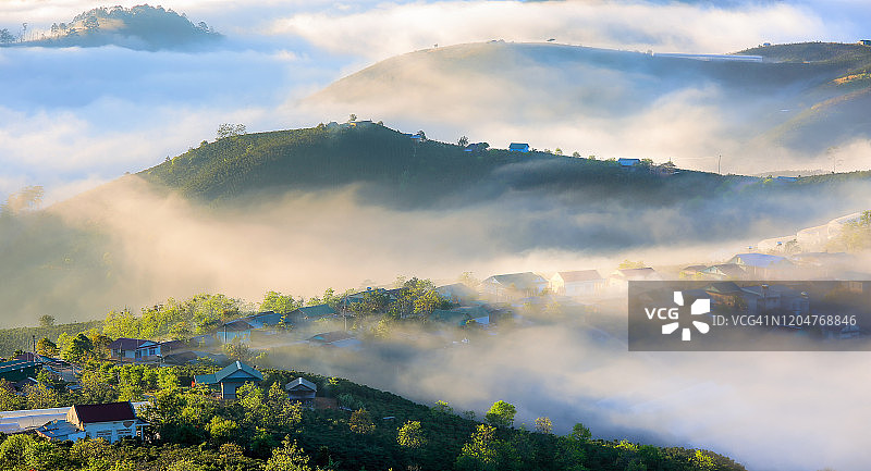 戏剧性的风景与美丽的小村庄隐藏在雾谷与神奇的光，雾蒙蒙和新鲜的风景在日出图片素材