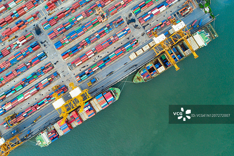 商业港口用岸吊在货轮上装载集装箱的鸟瞰图。集装箱船在进出口和业务物流与起重机和航运货物。国际运输与商务物流理念。图片素材