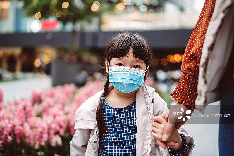 可爱的小女孩带着医用口罩和妈妈在公园散步图片素材