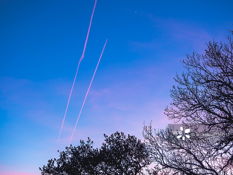 在冬天的森林里，夕阳全是彩色的，飞机在空中留下的痕迹图片素材