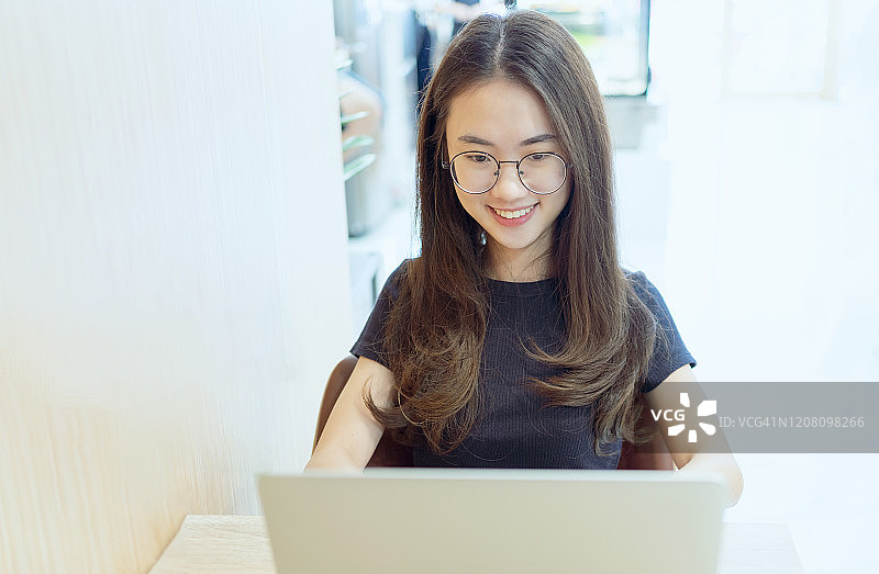 年轻的女商人在咖啡馆用笔记本电脑打字。微笑的女人坐在咖啡厅里用笔记本电脑工作。的生活方式。技术概念图片素材