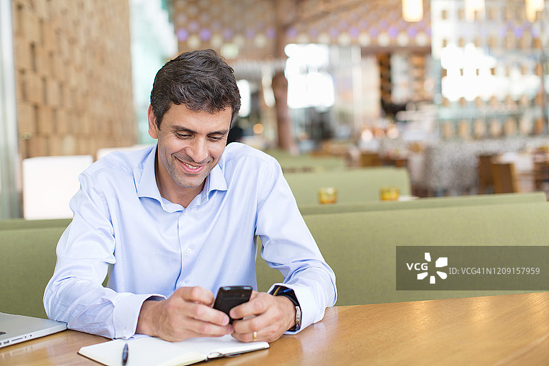 成熟的男人坐在酒店里，用手机，微笑着。图片素材