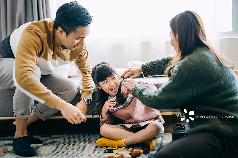 快乐的亚洲父母坐在客厅的地板上和女儿一起玩木制积木图片素材