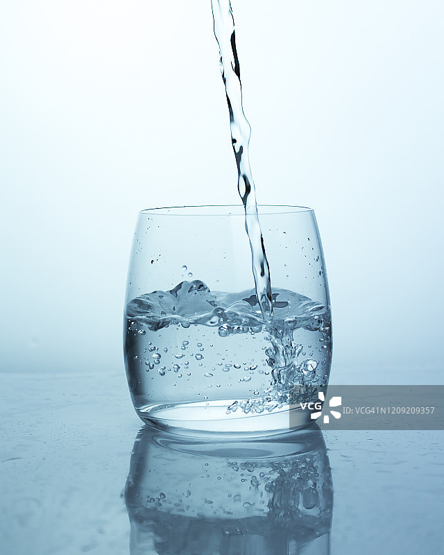 水柱飞溅而下落入玻璃杯中，玻璃杯中的水流产生气泡。水里有很多气泡图片素材