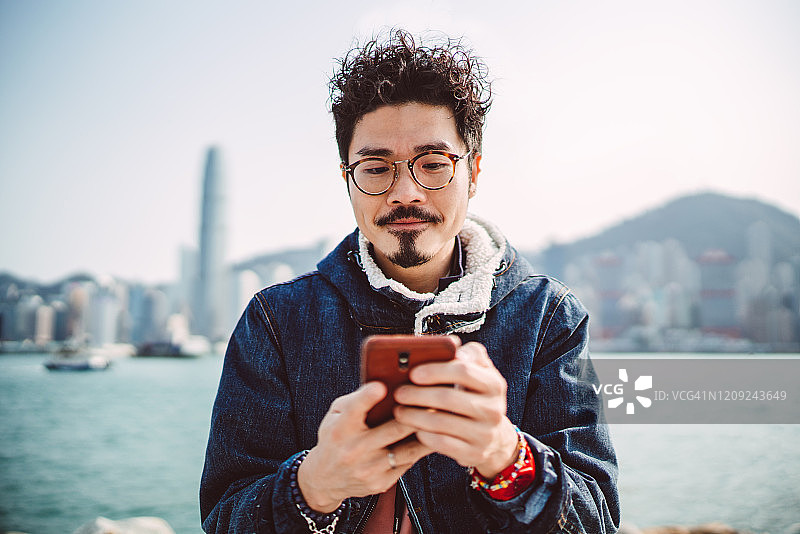 年轻的亚洲男子愉快地使用智能手机散步图片素材