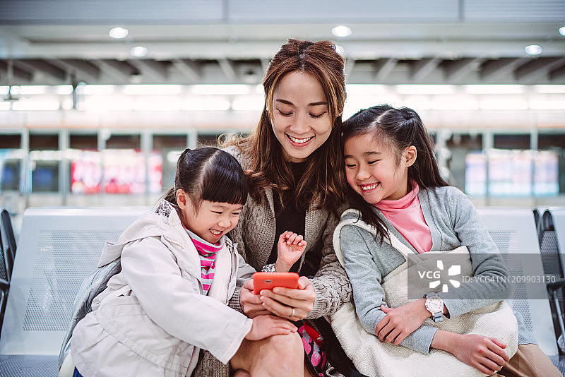 妈妈和女儿们愉快地在火车站台上使用智能手机图片素材