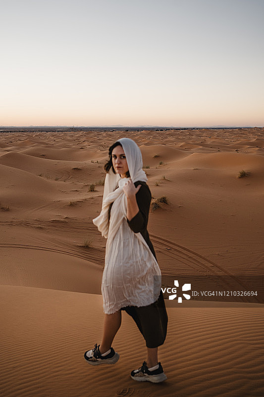 一名年轻女子戴着白色的头巾穿过沙漠图片素材