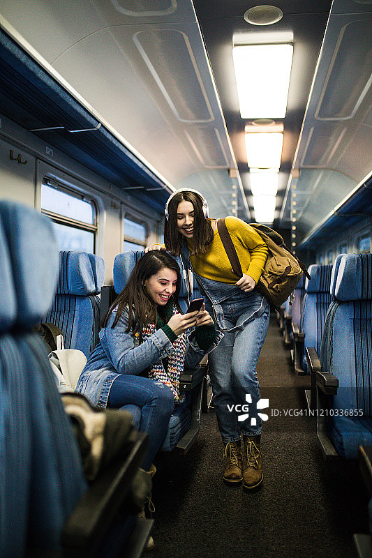几个女性朋友坐火车旅行，用智能手机看电视。图片素材