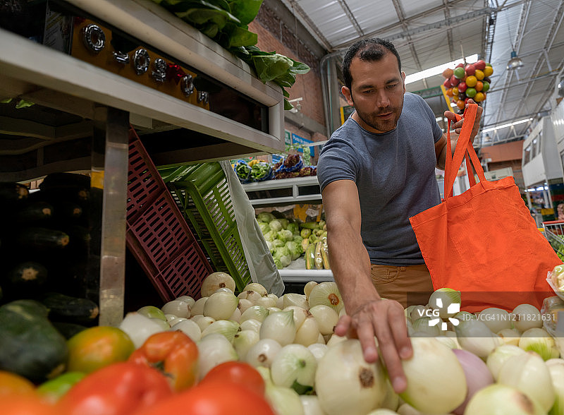 一名拉丁美洲男子使用可重复使用的袋子在售货亭购买蔬菜图片素材
