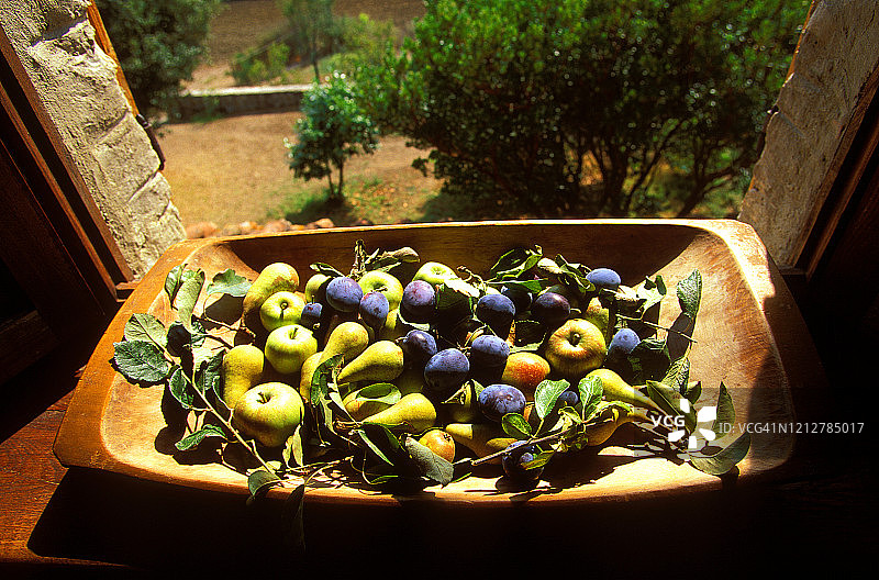 在意大利托斯卡纳的一扇开着的别墅窗户旁，一个古老的木果盘里装满了一堆新鲜采摘的苹果、李子和梨，还有树叶图片素材