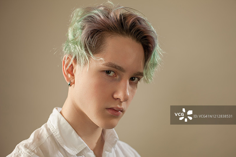 一个十几岁男孩的工作室肖像与绿色的头发在米色的背景图片素材