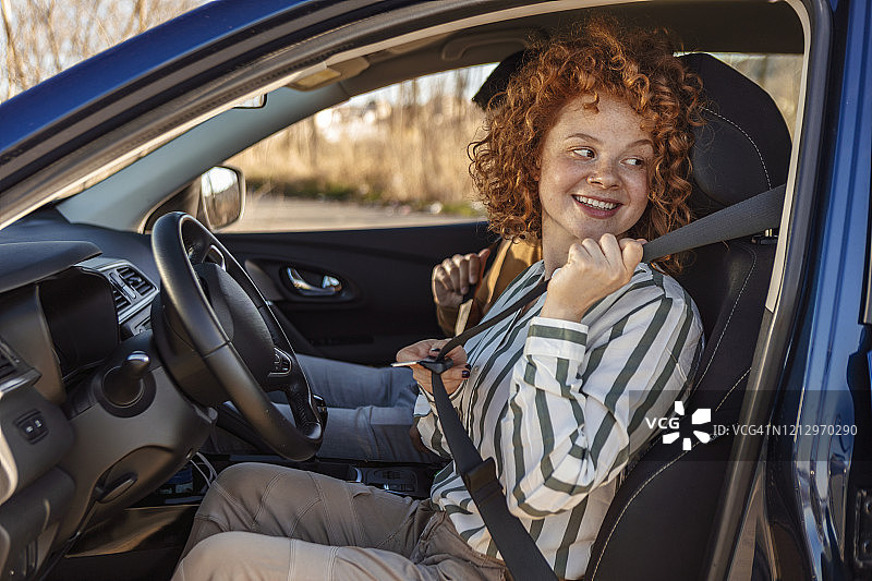 年轻的快乐美丽的女孩是系安全带在她的汽车的驾驶座图片素材