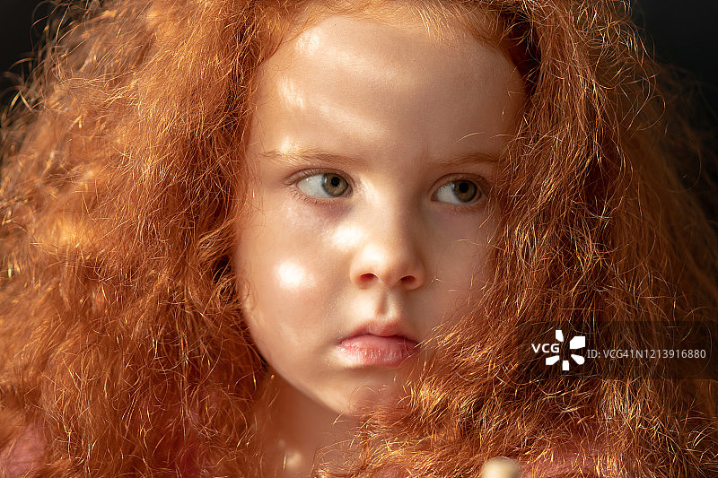 红发女婴特写肖像。明亮的阳光透过百叶窗。图片素材