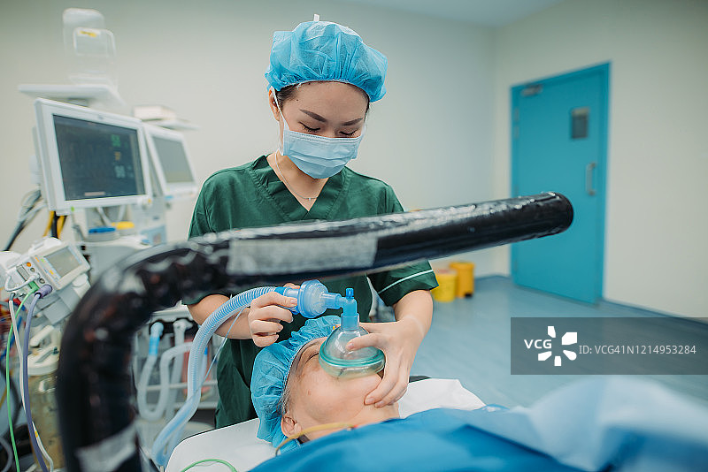 在医院的手术室里，年轻的亚洲华裔女医生给病人戴上氧气罩图片素材