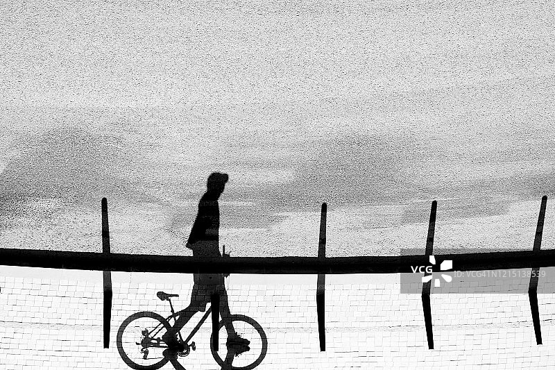 一个年轻人的影子剪影走和推着他的自行车，在黑色和白色图片素材