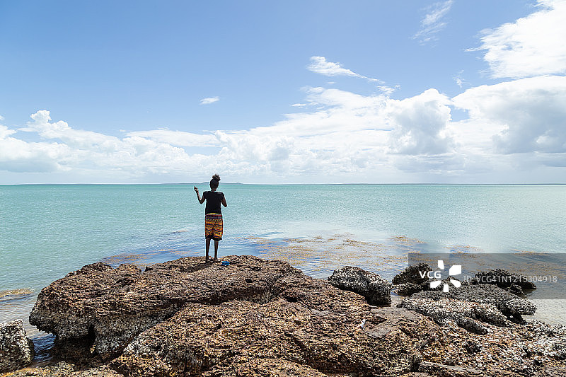 年轻的土著妇女站在岩石上在浩瀚的海洋中捕鱼图片素材