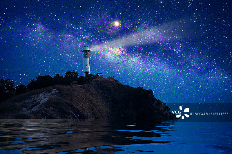 The lighthouse is on an island in an middle of The sea at night with many milky way and stars.灯塔位于大海中央的一座岛上，夜间有许多银河和星星。图片素材