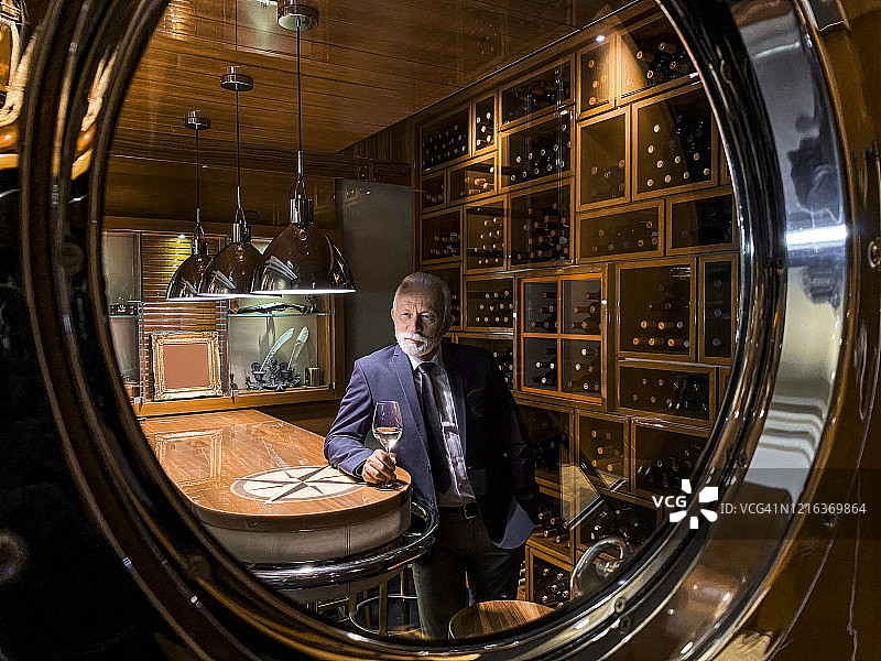 一个老富翁在游艇的酒窖的舷窗另一边品尝着白葡萄酒图片素材