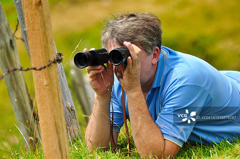 瑞士，一名男子躺在草地上，用双筒望远镜观看图片素材