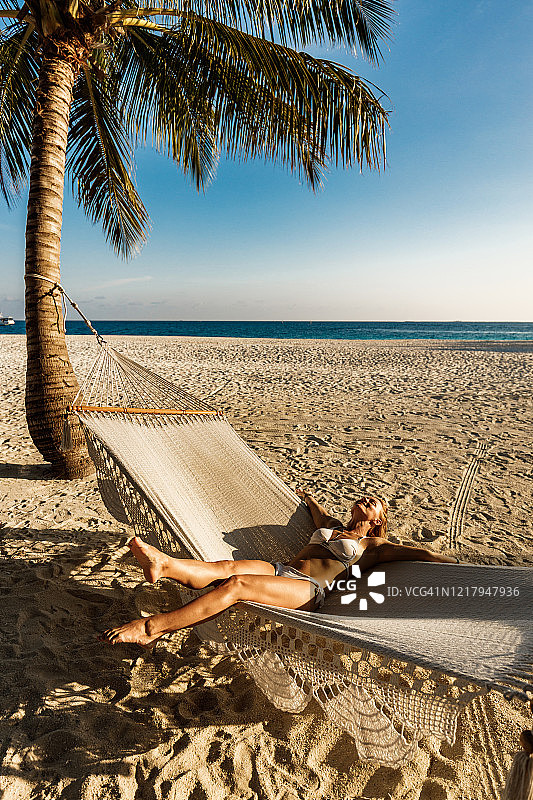 无忧无虑的女人在海滩吊床上享受她的夏日。图片素材