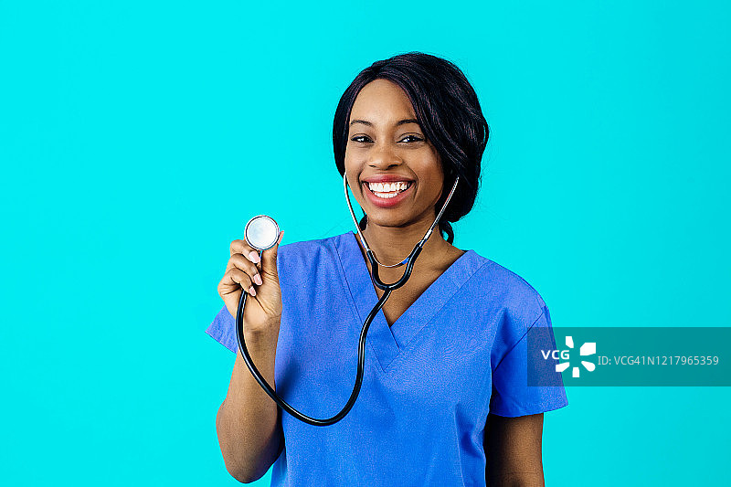 一个快乐和微笑的女医生或护士的肖像穿着蓝色的手术服，手持听诊器，孤立在蓝色的背景图片素材