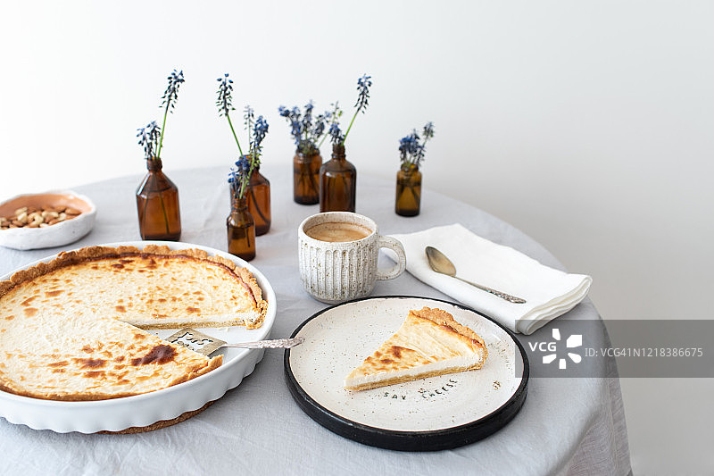 精美的早餐餐桌。天然和有机早餐美味的奶酪蛋糕，咖啡和鲜花亚麻桌布上的陶瓷餐具。图片素材