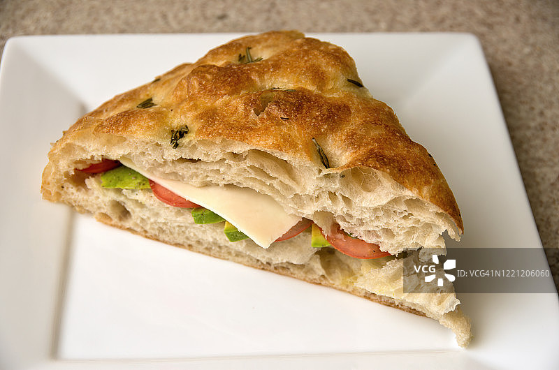 迷迭香佛卡夏面包三明治包含奶酪，番茄和鳄梨，在一个白色的盘子图片素材