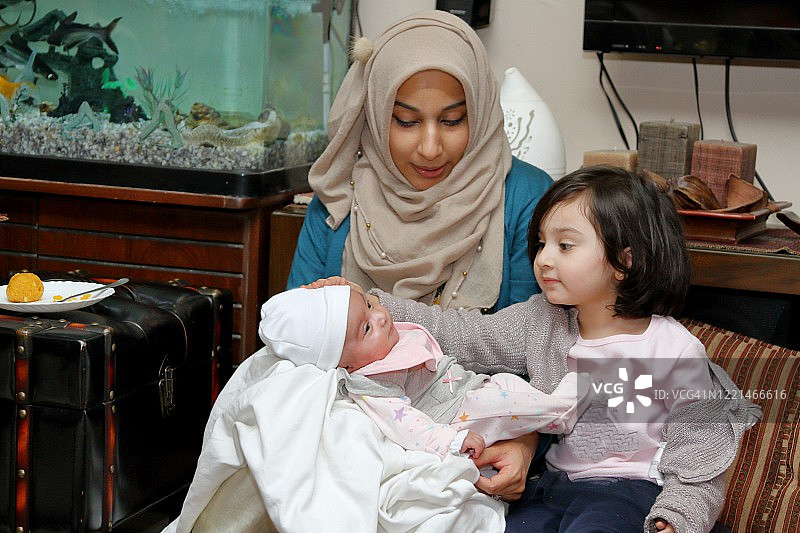 一位戴着面纱的母亲，膝盖上坐着两个女儿。图片素材