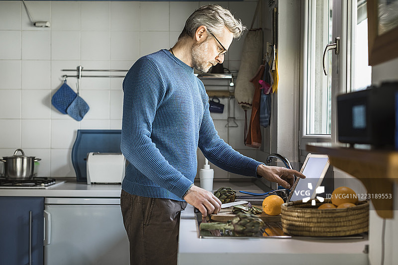 一个成熟的男人在厨房里用平板电脑准备洋蓟图片素材
