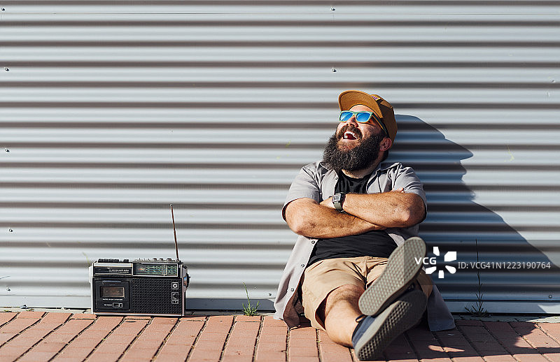 一幅蓄着胡须的男人拿着便携式收音机享受阳光的肖像图片素材