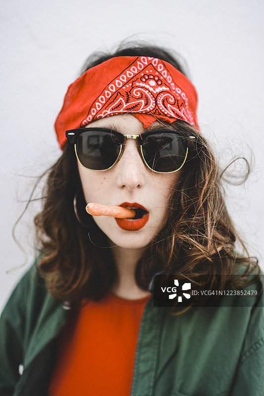 年轻女子的肖像戴着头巾和太阳镜抽着胡萝卜图片素材