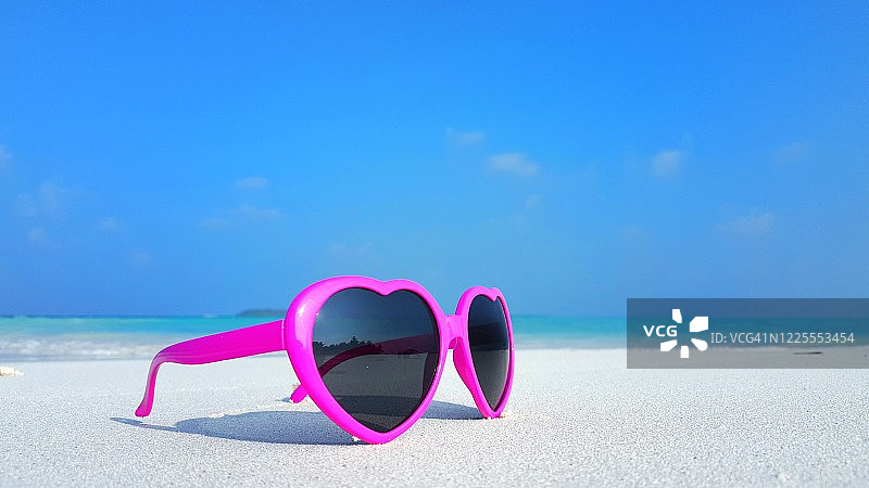 一对粉红色的太阳镜特写在一个充满异国情调的海滩与沙白色海岸图片素材