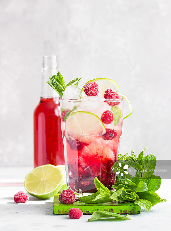 灰色的混凝土桌子上放着粉红色的鸡尾酒或柠檬水，配上覆盆子、薄荷、酸橙和冰。夏天点心饮料。图片素材