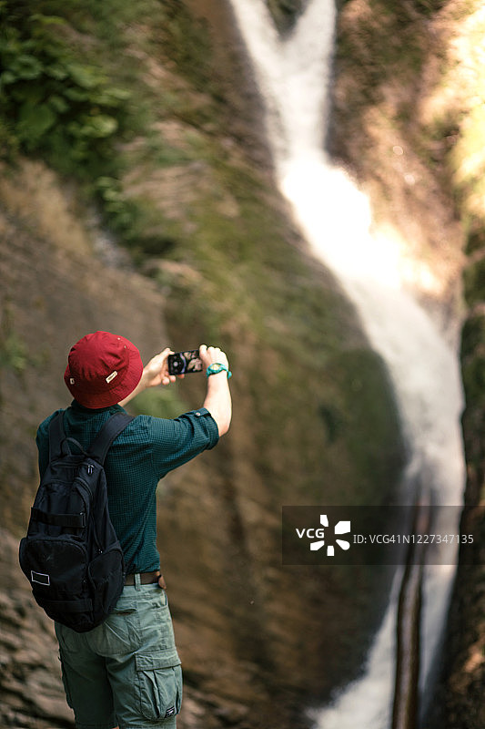 徒步者拿着智能手机试图在森林深处找到瀑布之间的联系。图片素材