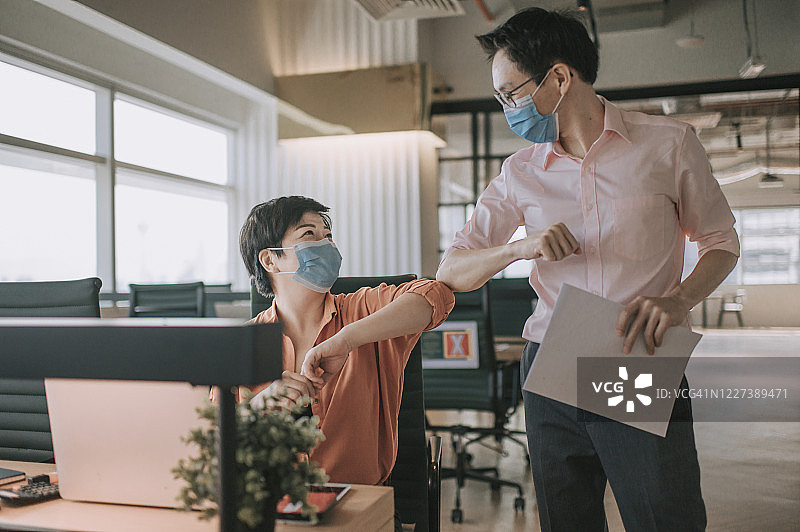 2 .亚洲华人同事在办公室用新的握手方式互相问候，戴上防护口罩图片素材