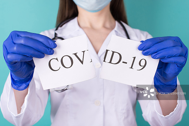 新型冠状病毒新冠病毒克服概念。专业医生戴着手套撕裂COVID-19纸的特写照片，隔离在蓝色绿松石背景图片素材