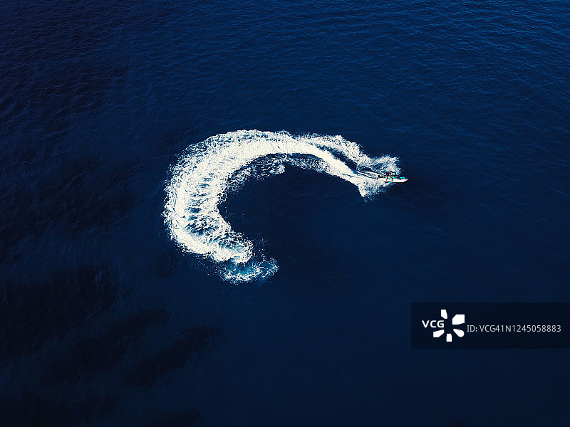 一艘喷气式快艇在深蓝色的海水中打旋的鸟瞰图。船的尾流从上面。图片素材