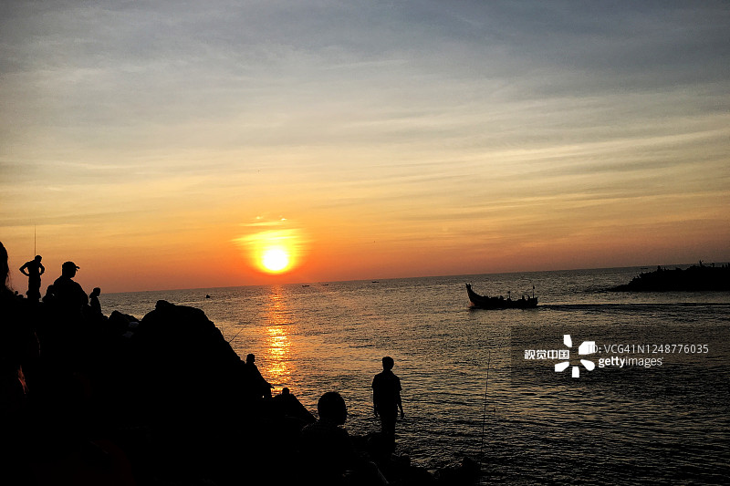 在印度喀拉拉邦，人们与渔船在海滩上观看日落的剪影景观图像。图片素材