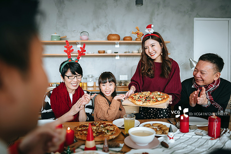 快乐的亚洲多代家庭花时间在一起庆祝圣诞节，微笑的年轻女子在圣诞节期间在家里为家人提供食物图片素材