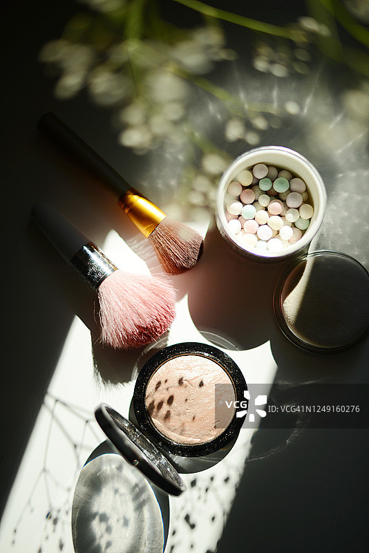 用高光笔和一个装有古铜色珍珠粉的罐子在白色背景上，可以在夏日早晨的阳光和阴影中看到图片素材