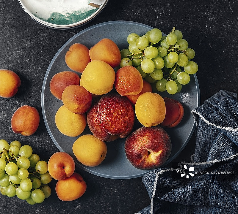 碗新鲜水果(葡萄，杏子和桃子)在黑色的背景图片素材