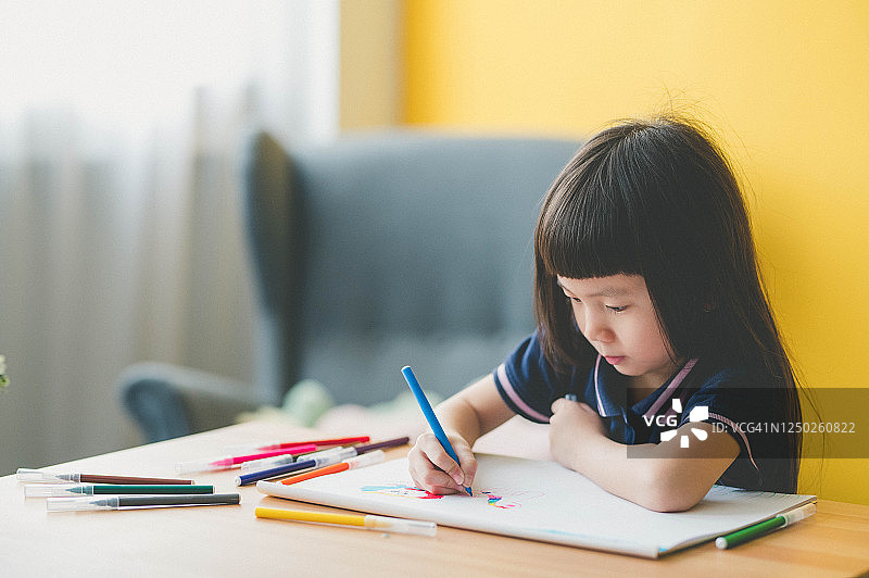甜美的亚洲小女孩坐在桌子上，用彩笔在客厅画画图片素材