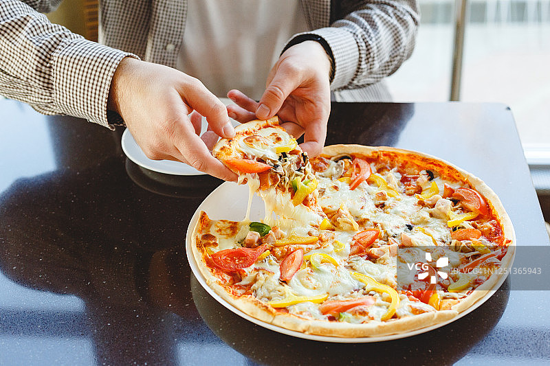 美味的披萨。一名白种人在咖啡馆、餐馆或家里拿着一块美味的意大利披萨，上面有马苏里拉奶酪。快餐的披萨图片素材