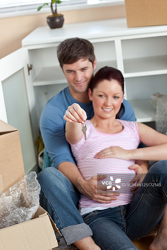 一对期待有孩子的快乐夫妇坐在地板上，手里拿着新房子的钥匙图片素材