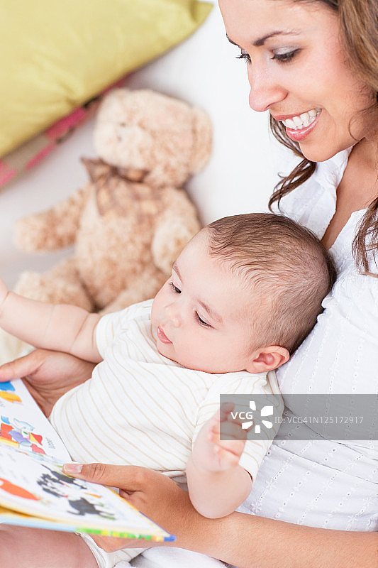 一张快乐的母亲坐在客厅里给她的孩子读书的肖像图片素材