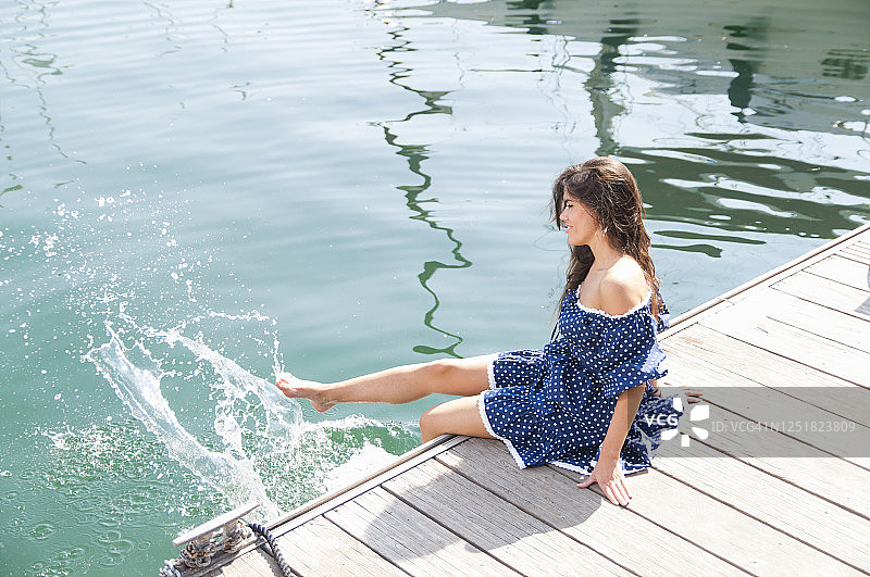 一名年轻女子坐在防波堤上，用腿向海里泼水图片素材
