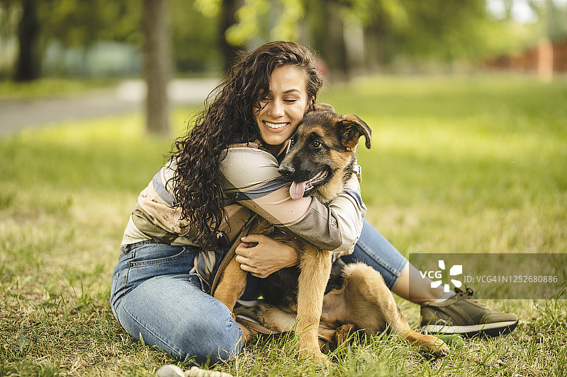 快乐的年轻女人和她的狗在公园草地上玩图片素材