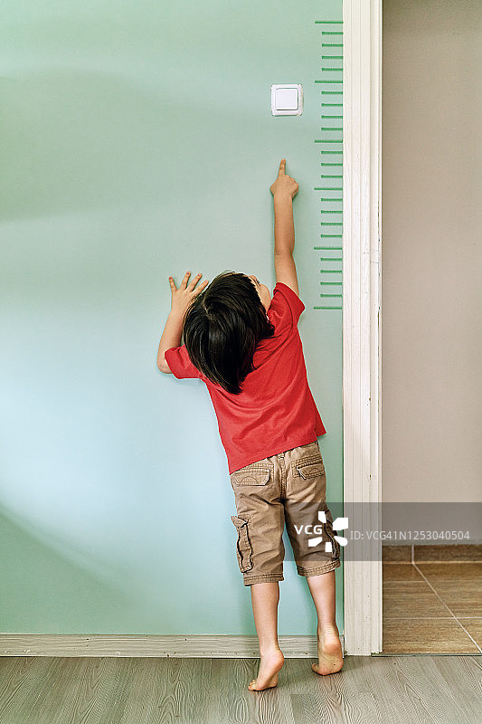 孩子在墙上测量自己的身高。他长得真快。图片素材
